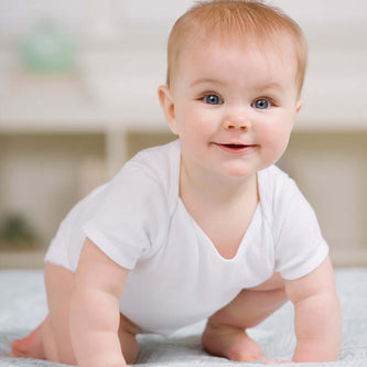 Happy baby in a white onesie crawling on a soft blanket, ideal for showcasing Baby Gift Sets.