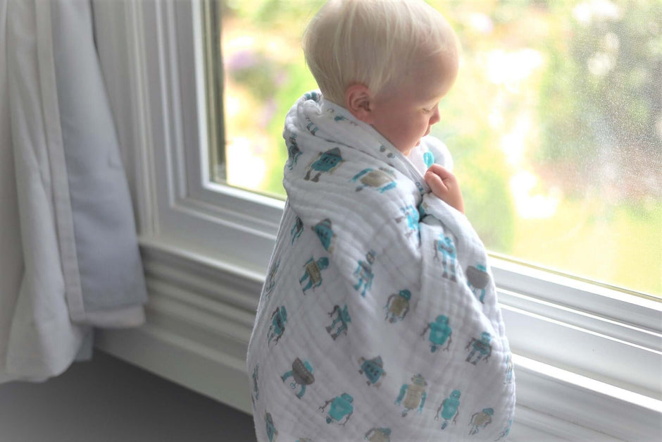 Cotton baby blanket wrapped around a child looking out the window, featuring playful robot designs.