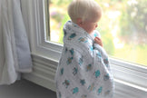 Cotton baby blanket wrapped around a child looking out the window, featuring playful robot designs.