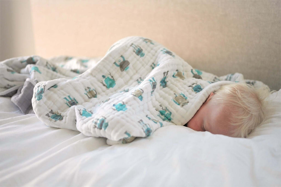 Cotton baby blanket wrapped around a sleeping infant on a bed.