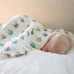 Cotton baby blanket wrapped around a sleeping infant on a bed.