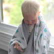 Cute toddler wrapped in a cotton baby blanket, playing by the window with soft natural light.