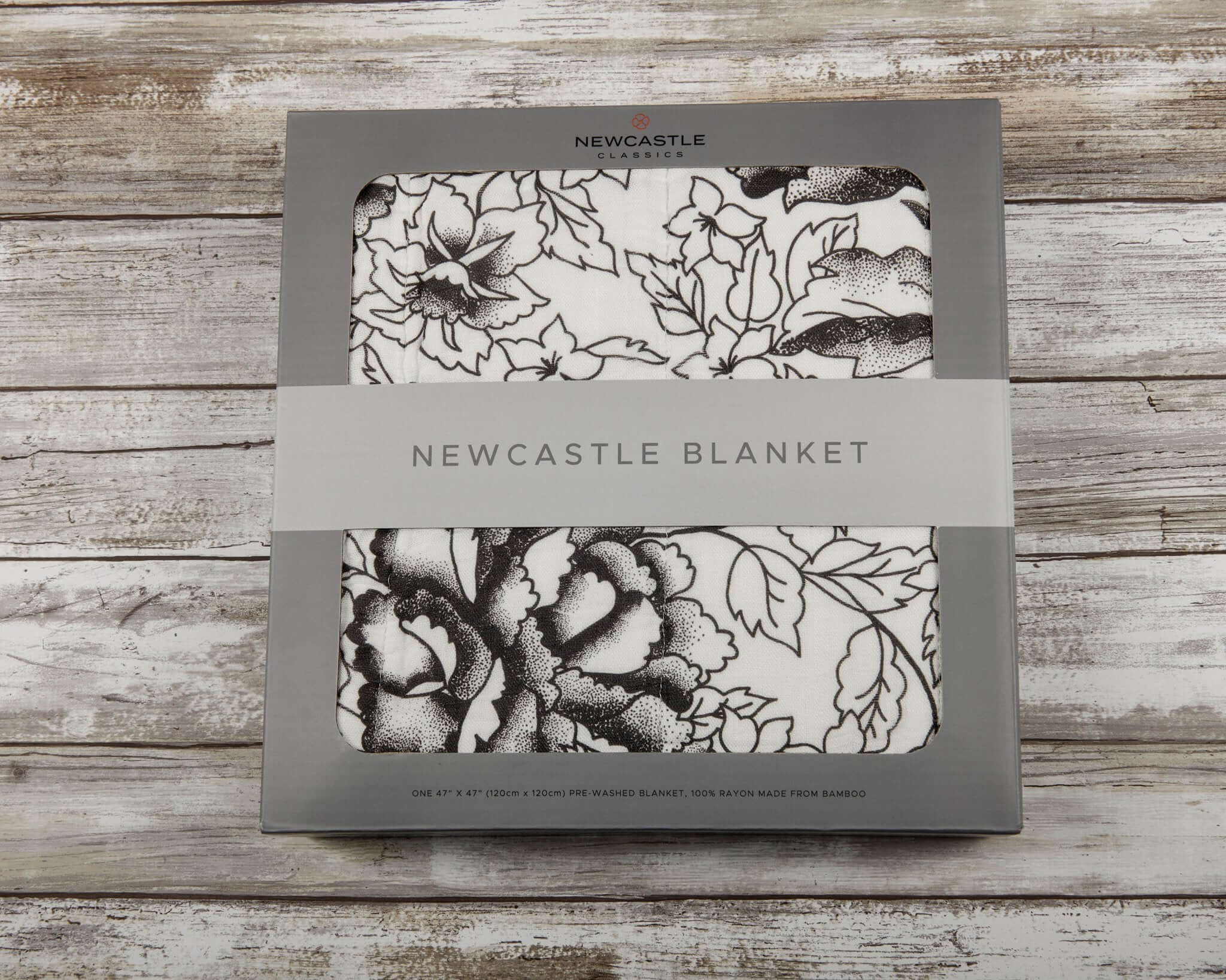 American Rose Newcastle Blanket packaging with floral design and brand logo on a rustic wooden background.