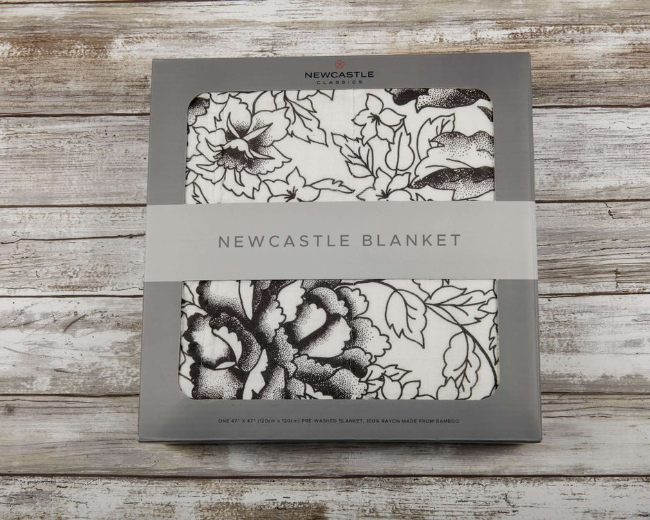 American Rose Newcastle Blanket packaging with floral design and brand logo on a rustic wooden background.