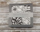 American Rose Newcastle Blanket packaging with floral design and brand logo on a rustic wooden background.