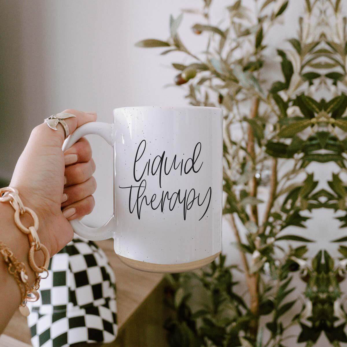 Person holding a Liquid Therapy Mug-16oz with a sleek design, surrounded by indoor plants.